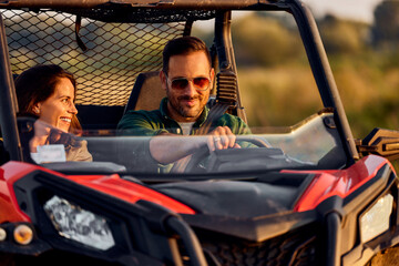 A smiling adult couple in love enjoying driving on a quad bike off-road.