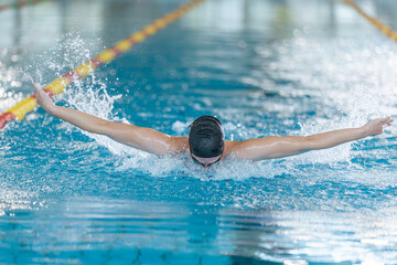 Female competitive swimmer moving through the water performing the butterfly stroke during swimming training, front view.