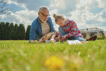 Focused child holding toy while playing with her grey haired grandfather at grassy lawn