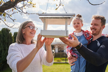 Happy man holding adorable little girl in his arms while kid looking at wooden birdhouse