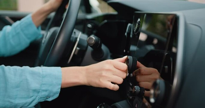 Young woman is sitting in the driver's seat using a touch display screen multimedia device in sporty car driven. Attaractive girl tasting new vehicle functions.