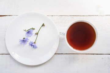 A top view of the cichorium flowers in a saucer, on a light background. A mug with a drink. Flowers of ordinary chicory or cichorium dioecious. With space to copy. High quality photo