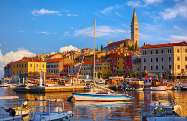 Rovinj, Croatia. Motorboats and boats on water in port of Rovigno. Medieval vintage houses of rovinj old town. Yachts landing, tower with clock. Morning sunrise in Istria with blue sky withclouds - 645038916