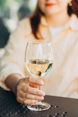 White wine glass in an outdoor cafe. Happy 30s woman sitting on the cafe terrace on the city street. Traveler. Woman hands toasting with wine