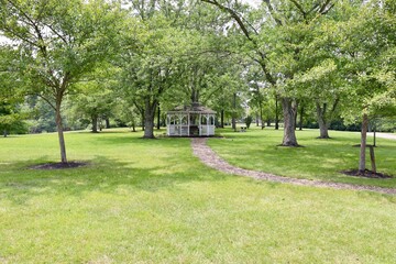 Fototapeta premium The white gazebo under the summer trees in the park.