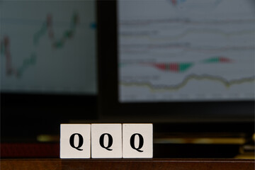 Financial image, "QQQ" ticker symbol in front of two computer screens, displaying financial graphs.