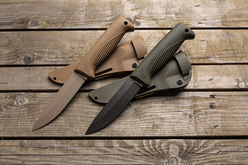 Modern hunting knives with rubberized handles and plastic sheaths. Melee weapons for hunting and self-defense. Vintage wooden back