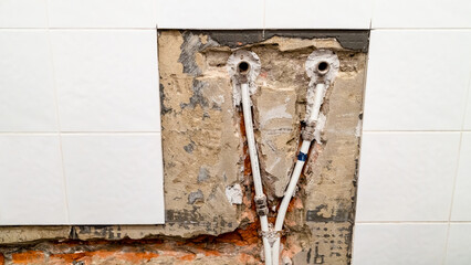 old water supply to faucet in bathroom and plumbing with metal-plastic pipes in chiseled brick wall under removed ceramic tiles