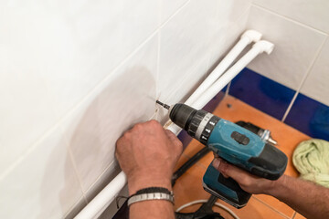 plumber drills hole for attaching new plastic pipes with drill in bathroom during installation of...