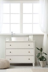 Interior of light bathroom with sink, pouf and houseplant