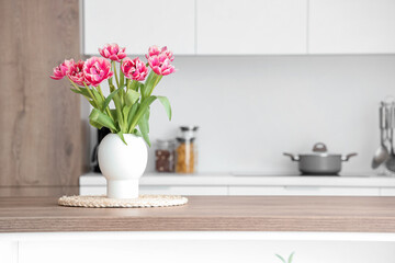 Vase with tulips on table in light kitchen