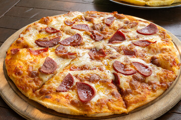 Pizza with cheese and sausage on a wooden serving plate
