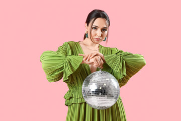 Fashionable beautiful woman in stylish green dress with disco ball posing on pink background