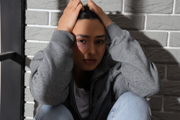 Bruised young woman near grey brick wall, closeup. Domestic violence concept