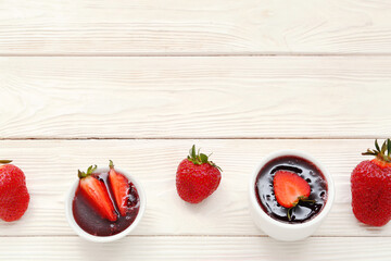 Bowls with sweet strawberry jam and fresh berries on white wooden background