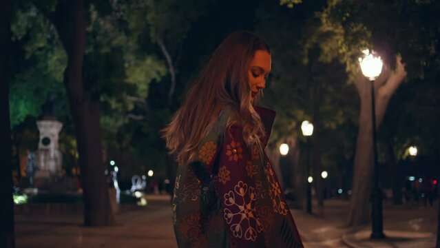Joyful girl walking dark city park at street lights close up. Model posing alley