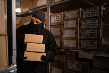 Thief in black balaclava steals with a parcel in a warehouse at the night. Concept of security...