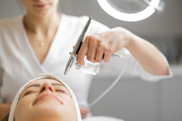 Young cosmetologist performs oxygen mesotherapy on woman's face at beauty salon. Concept of non-invasive and revitalizing skin treatment