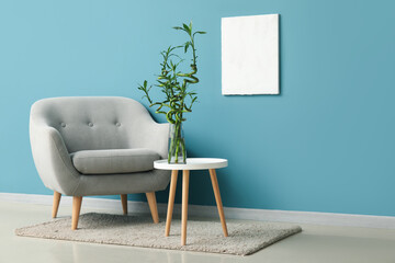 Comfortable armchair and bamboo stems on table near color wall