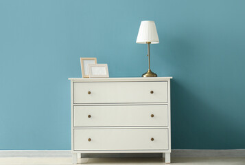 Blank picture frames and lamp on chest of drawers near color wall