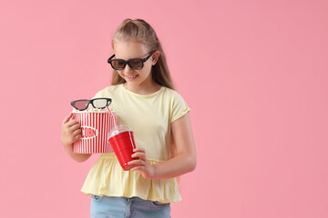 Happy little girl in 3D cinema glasses with popcorn bucket and cup of cola on pink background