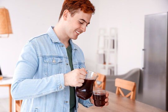 Young Man Pouring Juice Into Glass In Kitchen