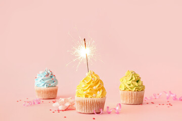 Tasty birthday cupcakes with sparkler and decor on pink background