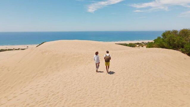couple travelers tourists walking sandy dunes on beautiful Patara Beach on Mediterranean sea coastline. stunning desert with dunes, mountain ridge and blue sea. beautiful popular spot in Turkey