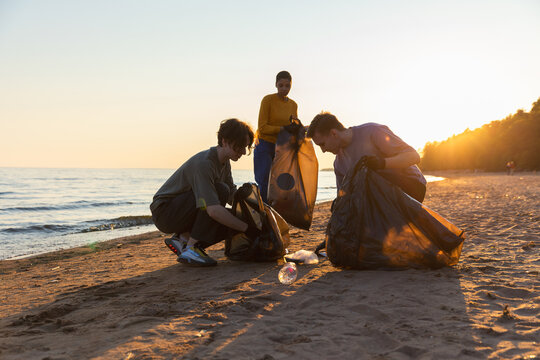 Earth day. Volunteers activists collects garbage cleaning of beach coastal zone. Woman and mans puts plastic trash in garbage bag on ocean shore. Environmental conservation coastal zone cleaning