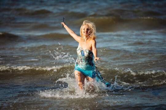 Happy blonde running along the seashore at sunset