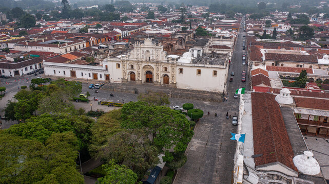 Templo iglesia del Santo Hermano Pedro de Antigua Guatemala fachada vieja antigua con plaza central con muchos &aacute;rboles con calles alrededor con casas y edificios al fondo