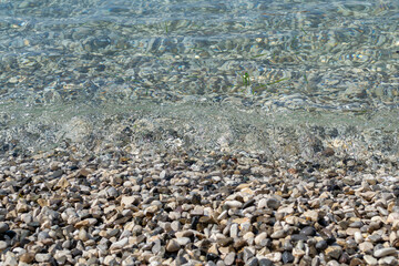 wave frozen in the moment near the shore, pebbles, clear water, sea