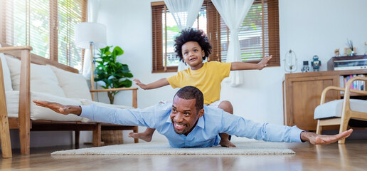 Portrait of African father and son play airplane flying on living room floor. Daddy and little boy spending leisure time together at home. Single dad, family lifestyle father's day concept