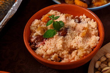 Couscous with dried fruits and nuts in a clay plate on the table.
