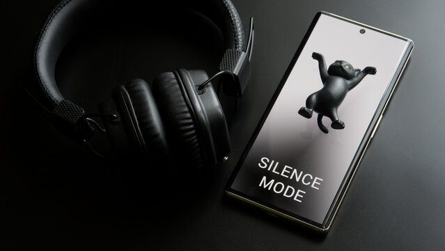 Mobile phone - a smartphone with activated silence mode and black wireless headphones next to a toy cat. Barring incoming calls and messages. Desire to be alone. Photo