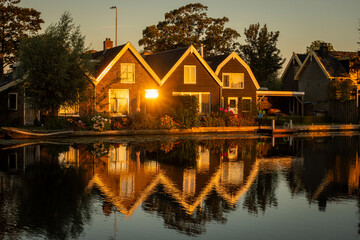 Obraz premium Traditional style Dutch architecture houses reflecting off the still water of the Oude Rijn river in the morning golden hour. riverside lifestyle with natural beauty for living comfort 
