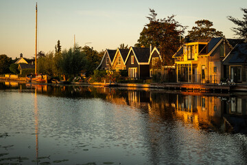 Traditional style Dutch architecture houses reflecting off the still water of the Oude Rijn river in the morning golden hour. riverside lifestyle with natural beauty for living comfort
