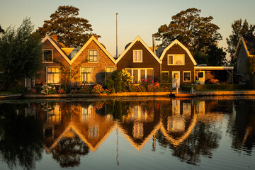 Fototapeta premium Traditional style Dutch architecture houses reflecting off the still water of the Oude Rijn river in the morning golden hour. riverside lifestyle with natural beauty for living comfort 
