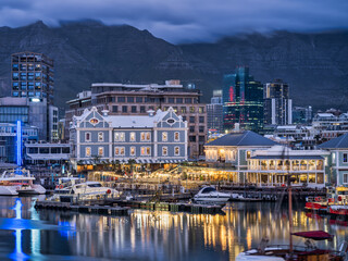 V and A Waterfront lit up with the table mountain in the background during a cloudy evening, Cape Town, South Africa