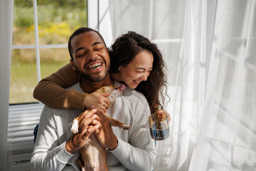 Joyful young interracial couple with morning coffee playing with chihuahua dog at home