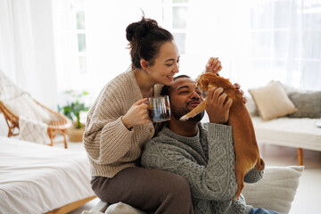 Cheerful young interracial couple with coffee playing with chihuahua dog at home - obrazy, fototapety, plakaty