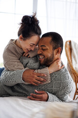 Cheerful young asian woman in sweater hugging african american boyfriend on bed at home