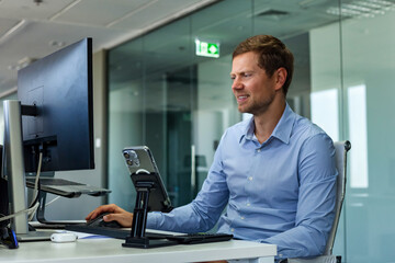 Smiling handsome man manager businessman works in corporate office. Confident male broker agent in blue shirt using pc computer at desk. Business development growth, career concept. Copy ad text space