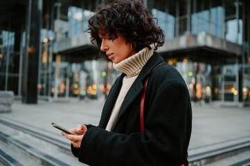 Pretty girl looking down to her smart phone while typing a text message on it.