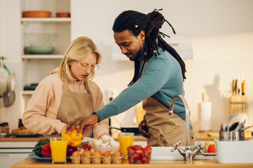 An interracial couple in love is cooking organic veggie food at home together.