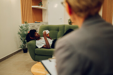 A depressed african american is lying down on the sofa and crying.