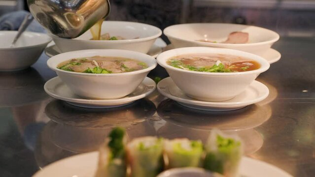 Bowls of pho with broth being poured in a restaurant kitchen, beef pho, Vietnamese food. 4K 24FPS