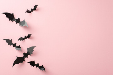 Fashion-forward Halloween concept. Top-down view snapshot showcasing flying bats on pastel pink setting. Ample room for greetings or advertisements
