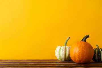 Embrace the harvest season! A side view shot of a wooden table adorned with a cornucopia of crops, including pumpkin and pattypans, set against orange wall backdrop