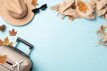 Autumn travel in style. Begin your journey with gray suitcase, luxurious cashmere scarf, stylish sunglasses and felt hat on light blue background, offering space for your promotional message or text